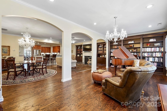 living room with dark hardwood / wood-style floors, built in features, crown molding, and ceiling fan with notable chandelier