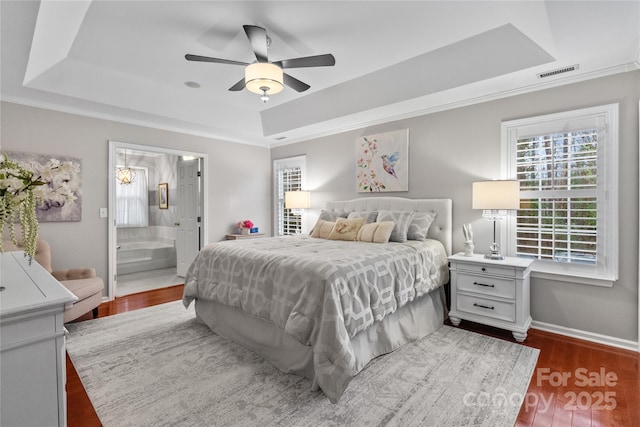 bedroom featuring ceiling fan, dark hardwood / wood-style floors, ensuite bathroom, and a tray ceiling