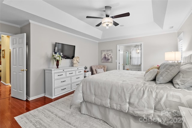 bedroom with crown molding, ensuite bath, ceiling fan, a tray ceiling, and dark hardwood / wood-style flooring