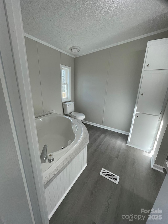 bathroom featuring a tub to relax in, toilet, hardwood / wood-style floors, and a textured ceiling