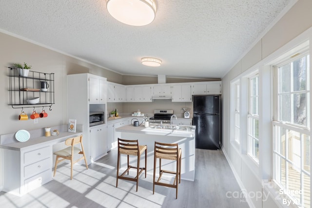 kitchen with appliances with stainless steel finishes, white cabinetry, a kitchen island with sink, vaulted ceiling, and a breakfast bar area