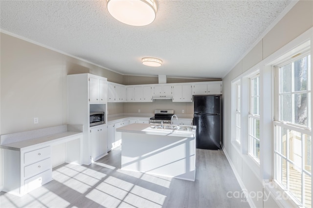 kitchen featuring a textured ceiling, appliances with stainless steel finishes, white cabinetry, a kitchen island with sink, and vaulted ceiling