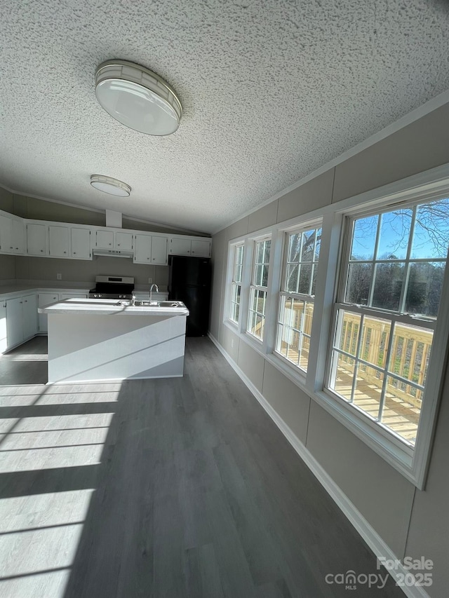 kitchen featuring white cabinetry, dark hardwood / wood-style flooring, stainless steel stove, black fridge, and a kitchen island with sink