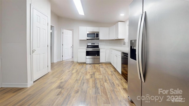 kitchen with tasteful backsplash, light hardwood / wood-style floors, vaulted ceiling, white cabinets, and appliances with stainless steel finishes