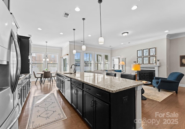 kitchen with appliances with stainless steel finishes, light stone counters, sink, a center island with sink, and hanging light fixtures