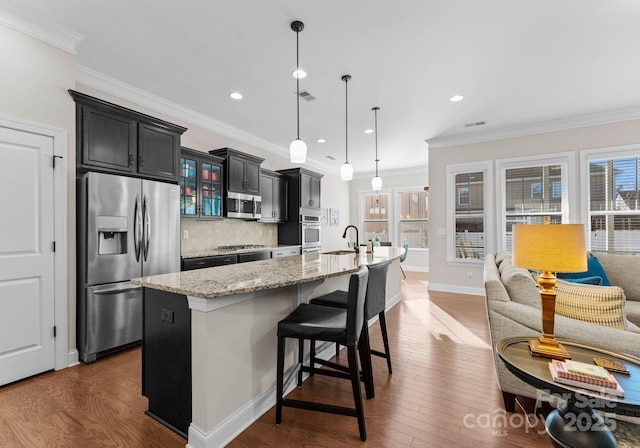 kitchen featuring sink, an island with sink, tasteful backsplash, decorative light fixtures, and stainless steel appliances