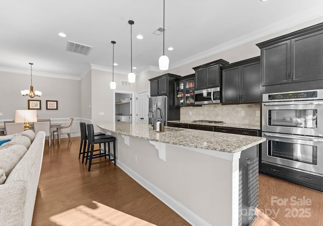 kitchen with decorative light fixtures, stainless steel appliances, a kitchen breakfast bar, and a center island with sink