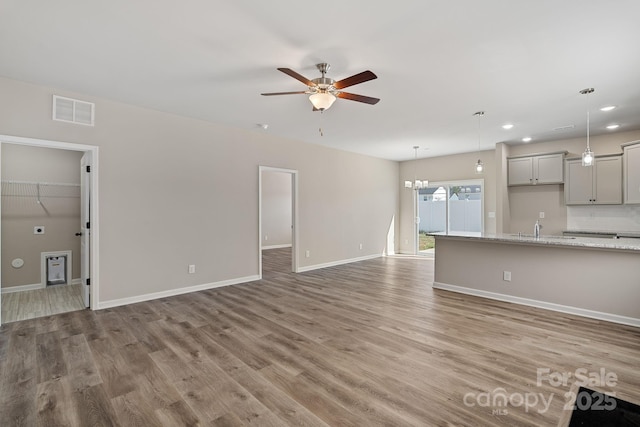 unfurnished living room with ceiling fan with notable chandelier, wood-type flooring, and sink