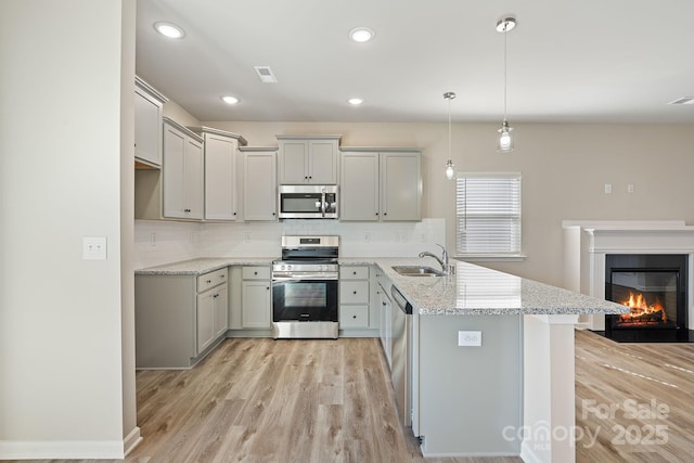 kitchen with light stone counters, stainless steel appliances, sink, pendant lighting, and gray cabinets