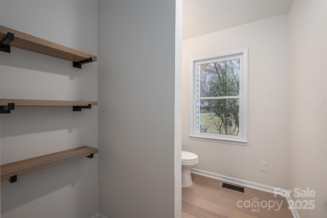 bathroom with wood-type flooring, toilet, and a healthy amount of sunlight