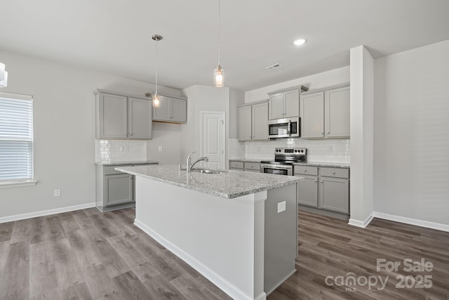 kitchen with a center island with sink, sink, gray cabinets, light stone countertops, and stainless steel appliances