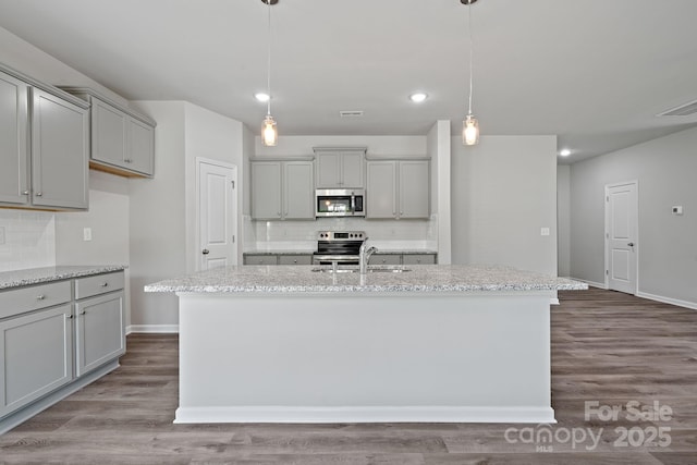 kitchen with appliances with stainless steel finishes, a kitchen island with sink, and gray cabinetry