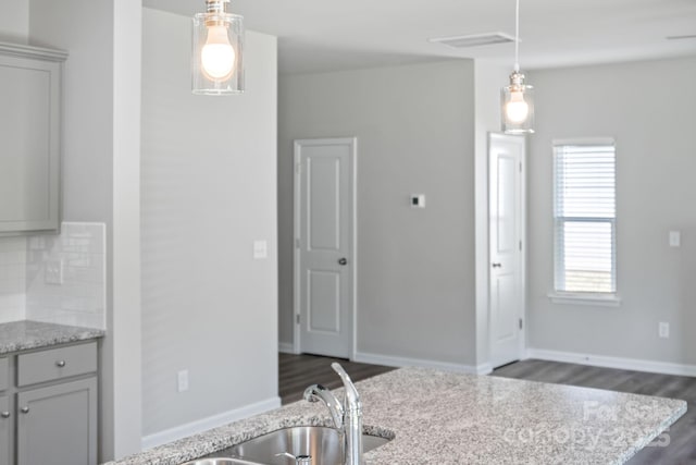 kitchen with light stone countertops, gray cabinetry, decorative backsplash, and pendant lighting