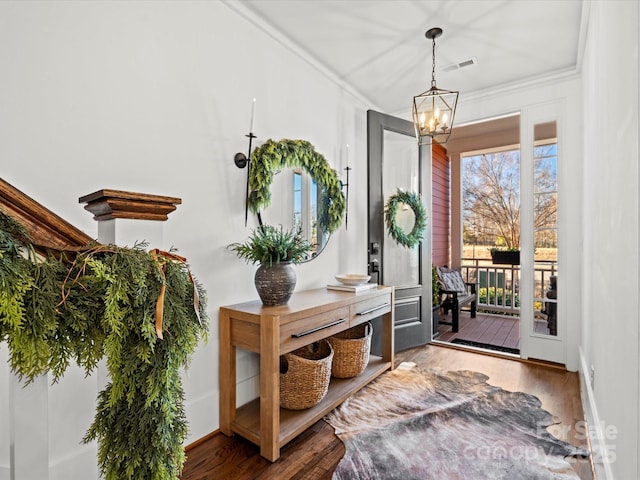 entrance foyer with an inviting chandelier, wood-type flooring, and ornamental molding