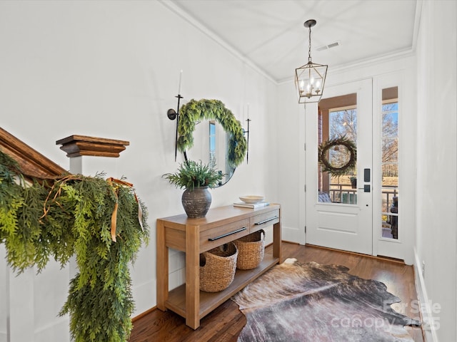 foyer entrance with ornamental molding, an inviting chandelier, and dark wood-type flooring