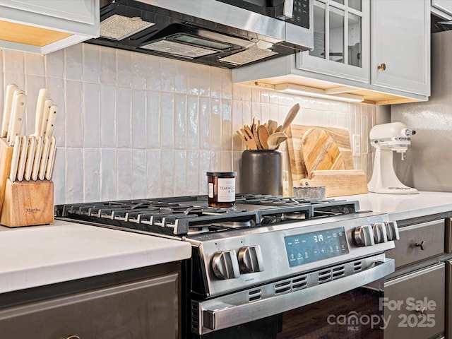 interior details featuring decorative backsplash, white cabinetry, and appliances with stainless steel finishes