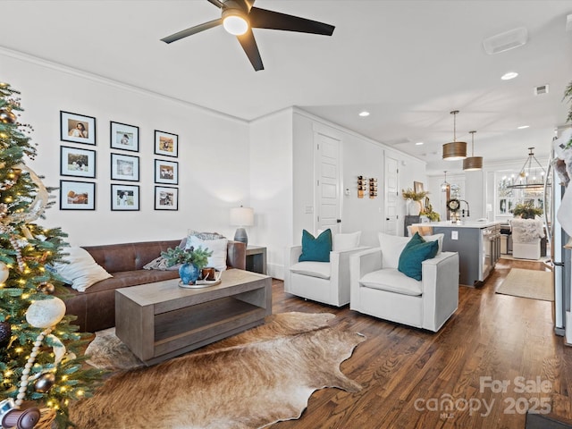 living room with dark hardwood / wood-style floors, ornamental molding, and ceiling fan with notable chandelier