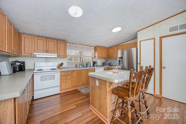 kitchen featuring white appliances, a kitchen island, vaulted ceiling, hardwood / wood-style flooring, and a breakfast bar area