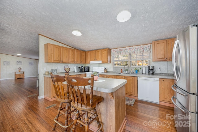 kitchen with white appliances, a kitchen island, a kitchen bar, dark wood-type flooring, and sink