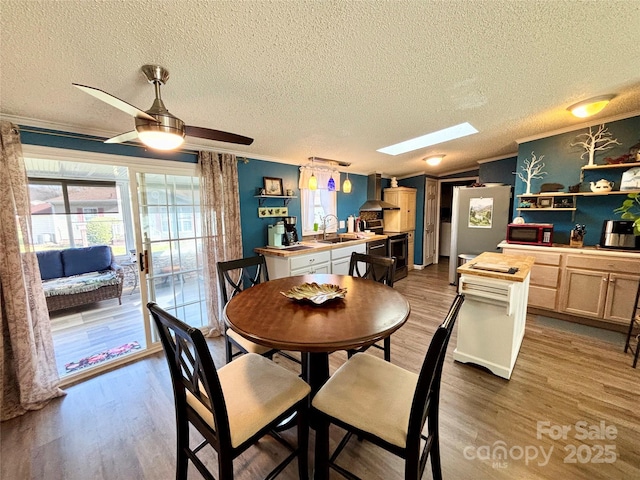 dining area featuring ceiling fan, light wood-type flooring, ornamental molding, and a skylight