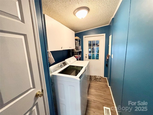 laundry area with washing machine and clothes dryer, cabinets, light hardwood / wood-style floors, a textured ceiling, and ornamental molding