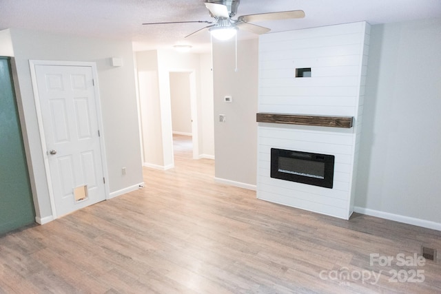 unfurnished living room with light wood-type flooring, ceiling fan, a textured ceiling, and a fireplace