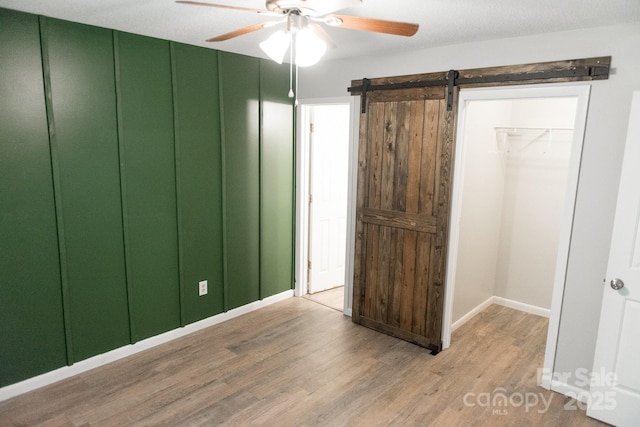 unfurnished bedroom featuring ceiling fan, a barn door, and light hardwood / wood-style flooring