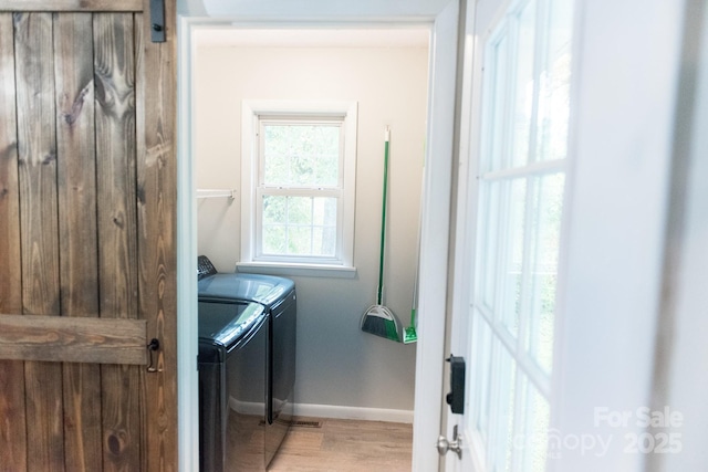 clothes washing area with washing machine and dryer, a barn door, and light wood-type flooring