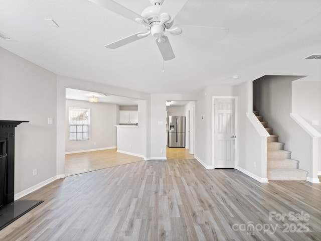 unfurnished living room with stairs, light wood finished floors, and visible vents