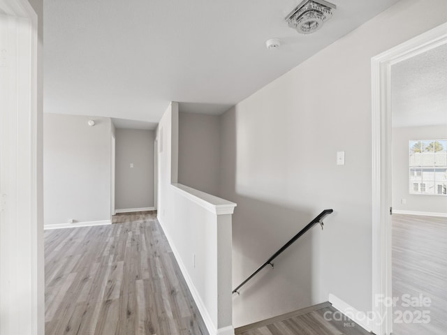 corridor with baseboards, light wood finished floors, an upstairs landing, and a textured ceiling