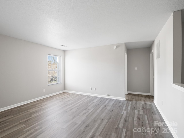 empty room with visible vents, a textured ceiling, baseboards, and wood finished floors