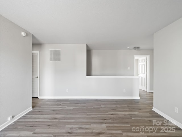 unfurnished room with wood finished floors, visible vents, and baseboards