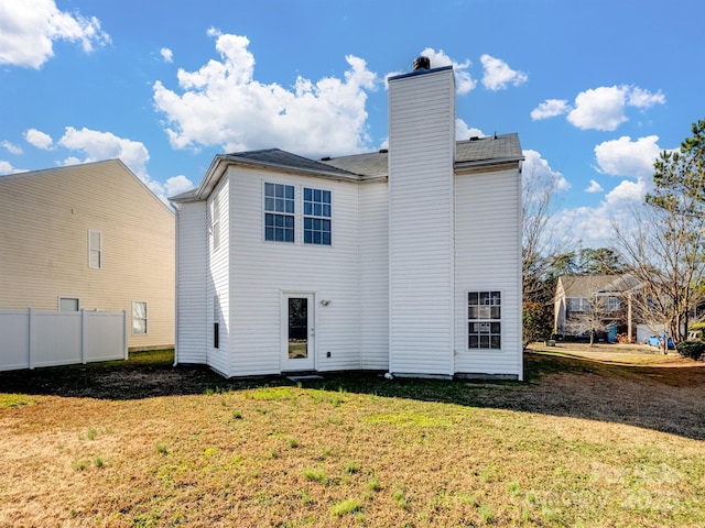 rear view of property featuring a yard, fence, and a chimney