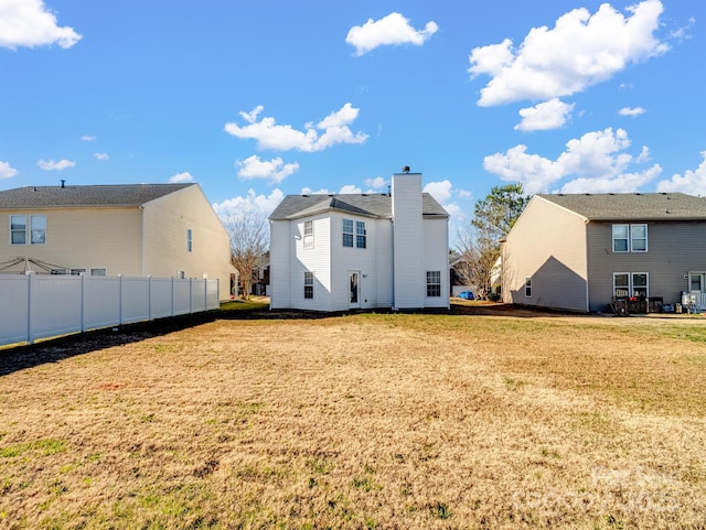 back of property featuring a lawn, a chimney, and fence