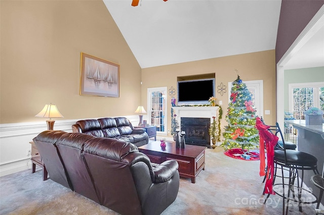 carpeted living area with a fireplace with flush hearth, high vaulted ceiling, and a ceiling fan