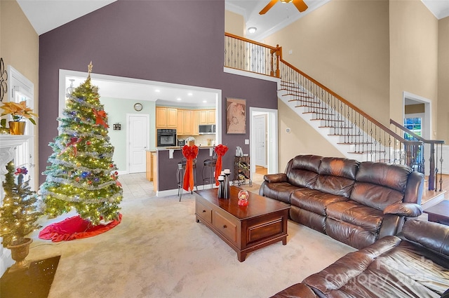 living area featuring stairs, ceiling fan, a towering ceiling, and light colored carpet