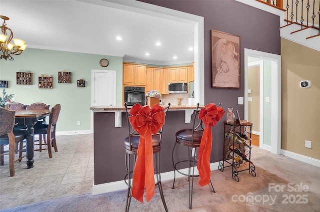 kitchen featuring a breakfast bar, black oven, light brown cabinetry, stainless steel microwave, and an inviting chandelier