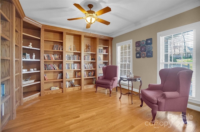 sitting room with ornamental molding, light wood-type flooring, baseboards, and a ceiling fan