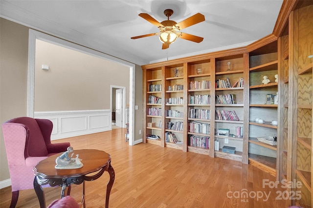 living area featuring a decorative wall, a wainscoted wall, wood finished floors, a ceiling fan, and ornamental molding