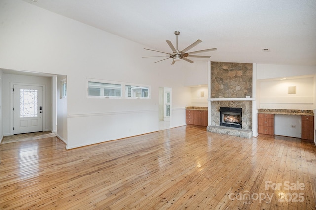 unfurnished living room featuring ceiling fan, high vaulted ceiling, a fireplace, and light hardwood / wood-style floors