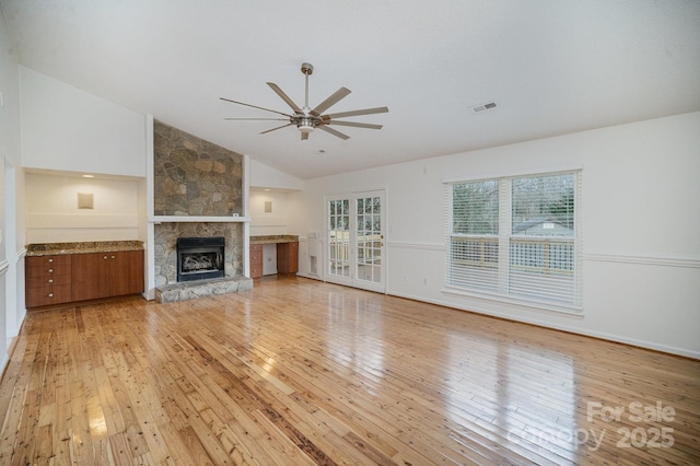 unfurnished living room with ceiling fan, a stone fireplace, lofted ceiling, and light hardwood / wood-style flooring