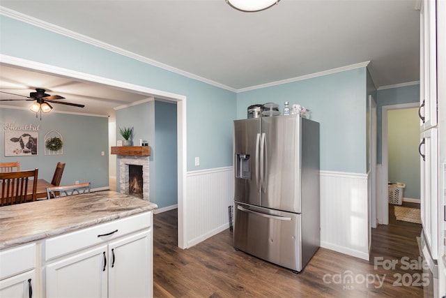 kitchen featuring stainless steel fridge, ornamental molding, ceiling fan, a fireplace, and white cabinetry