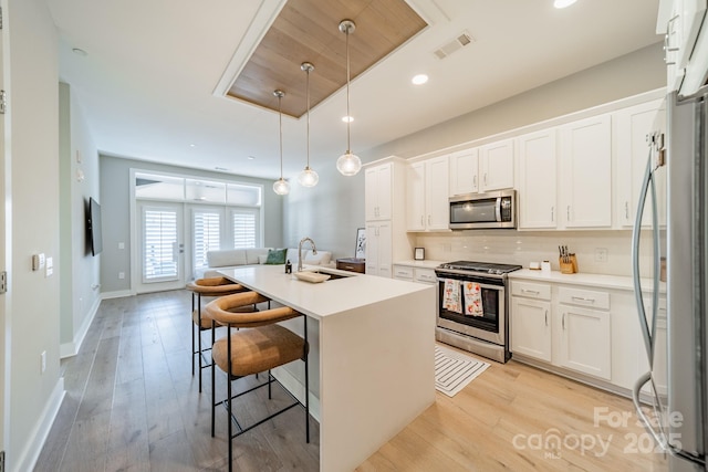 kitchen with white cabinets, sink, stainless steel appliances, and an island with sink