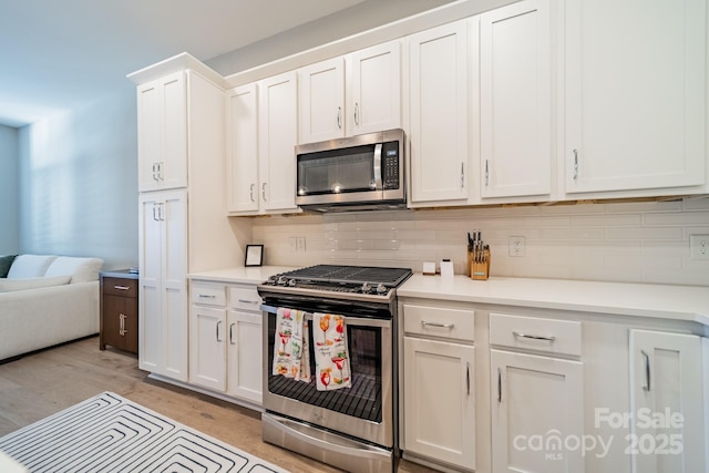 kitchen with white cabinets, appliances with stainless steel finishes, backsplash, and light hardwood / wood-style flooring