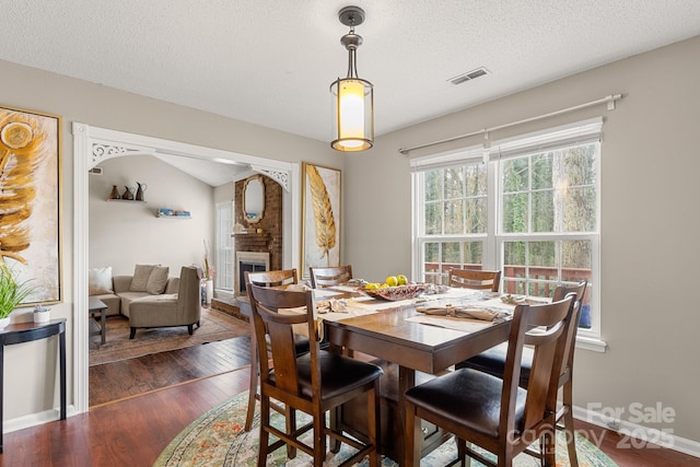 dining space with vaulted ceiling, dark wood-type flooring, a textured ceiling, and a brick fireplace