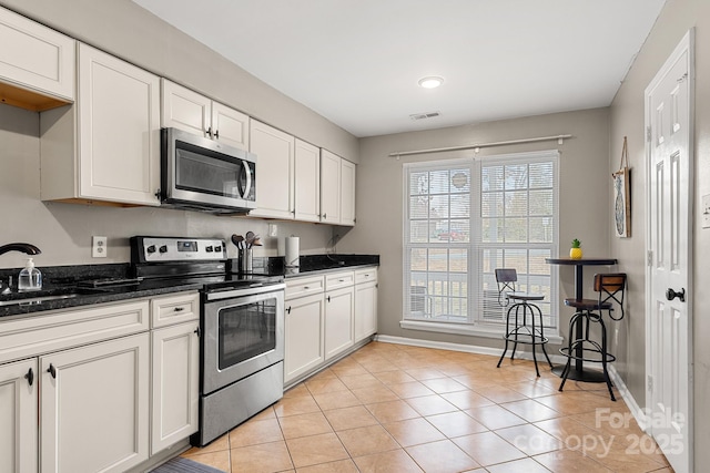 kitchen featuring white cabinets, light tile patterned floors, appliances with stainless steel finishes, and dark stone counters