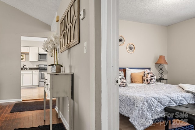 bedroom featuring sink, wood-type flooring, a textured ceiling, and vaulted ceiling