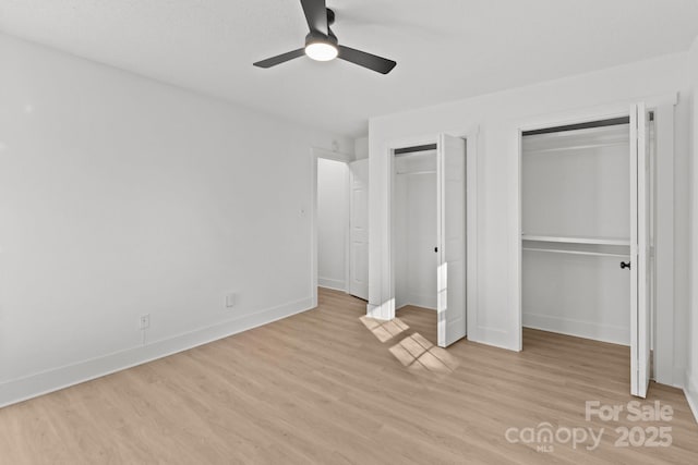 unfurnished bedroom featuring ceiling fan, two closets, and light wood-type flooring