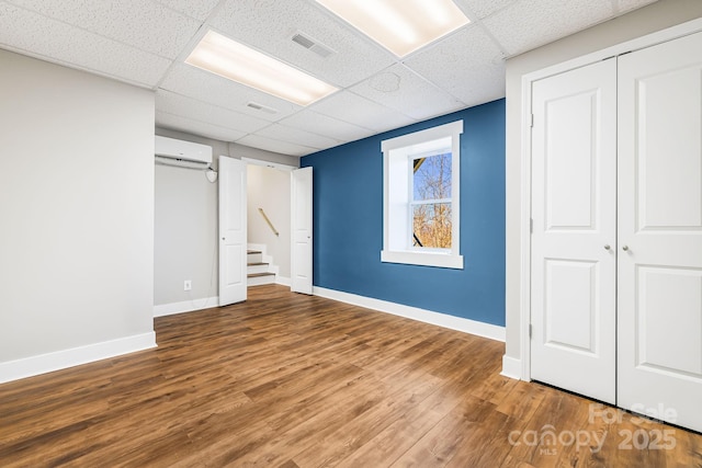 basement featuring wood-type flooring, a paneled ceiling, and a wall mounted AC