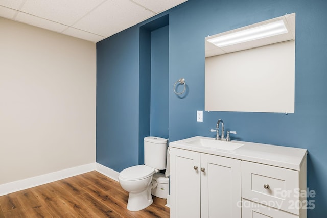 bathroom with a paneled ceiling, hardwood / wood-style flooring, vanity, and toilet